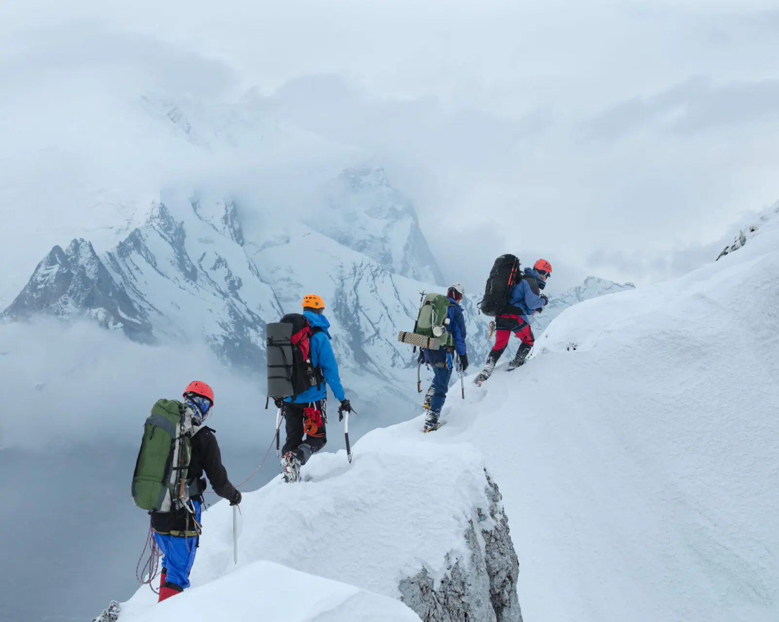 Team of mountain climbers walking on narrow ridge in winter scenery